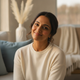 Headshot of a smiling South Asian woman, late 30s, with a calm and content expression, against a blurred background with blue